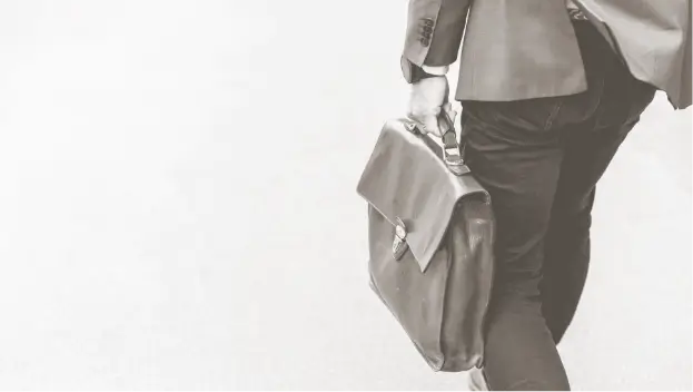 A professional in a suit with leather briefcase, walking away from the viewer