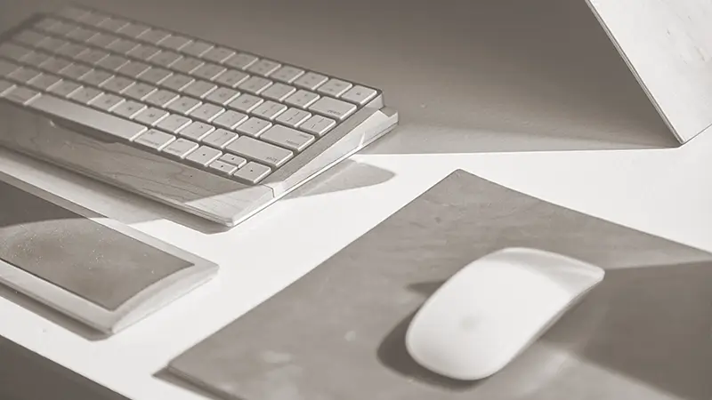 An image of a clean modern workspace desktop with mac keyboard and mouse on a leather mouse surface